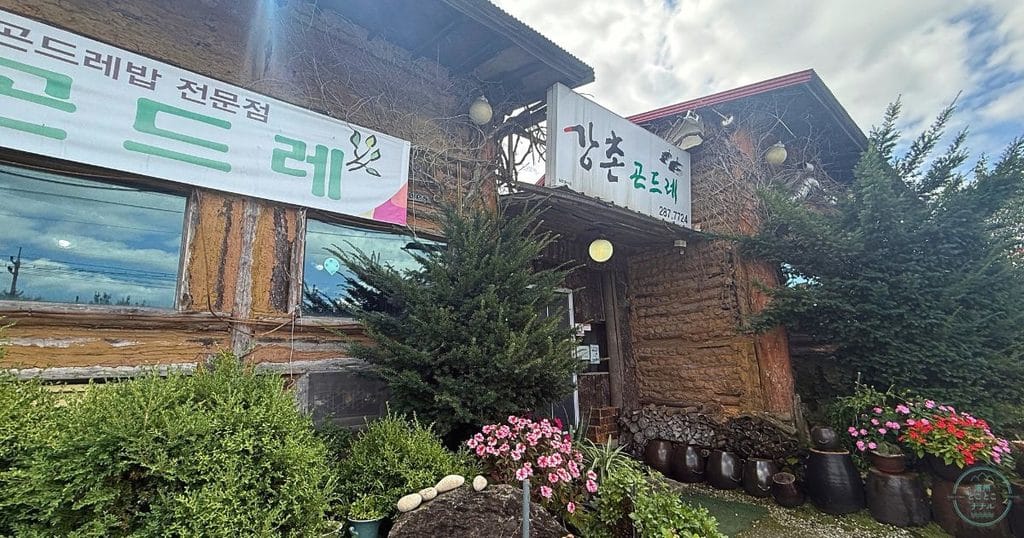韓国・清州(청주 )가덕면の강촌곤드레(カンチョン コンドゥレ)の外観。丸太と土壁の山小屋風の建物と「곤드레밥 전문점」の横断幕